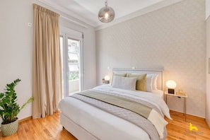 Ein Schlafzimmer mit einem großen Bett, einem Blumentopf, einem Nachttisch mit Lampe und Blick ins Freie durch eine Schiebetür.