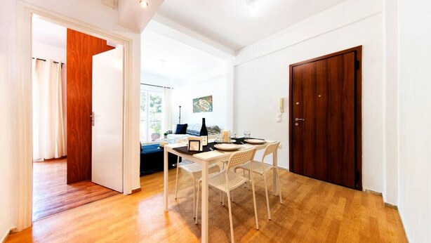 A dining area with a wooden table and chairs, a bottle, and a painting on the wall. - Acropolis Hillside Escape, Sea & Nature Views (Athina)
