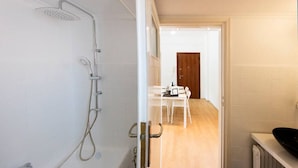 A modern bathroom with a shower, a sink, and a wooden door leading to a dining area. - Acropolis Hillside Escape, Sea & Nature Views (Athina)