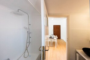 Ein modernes Badezimmer mit Dusche, Waschbecken und einer Holztür, die in einen Essbereich führt.