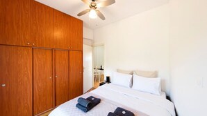 A bedroom with a large wooden wardrobe, a bed with white bedding, and a ceiling fan. - Acropolis Hillside Escape, Sea & Nature Views (Athina)