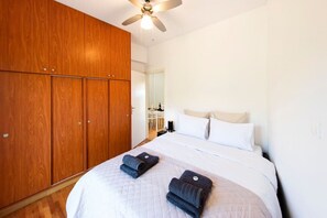Ein Schlafzimmer mit großem Holzschrank, einem Bett mit weißer Bettwäsche und einem Deckenventilator.
