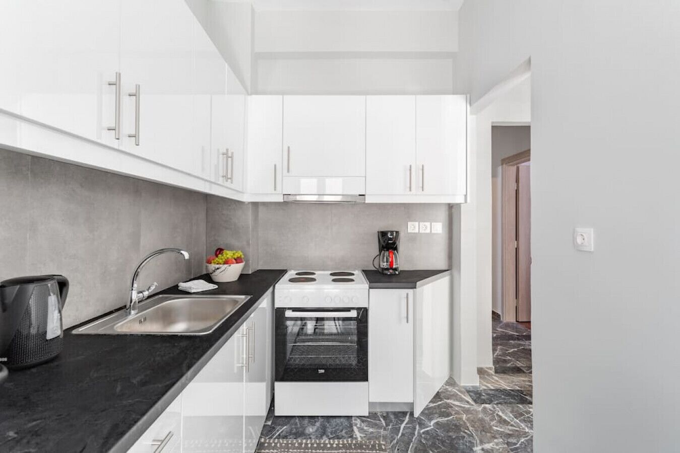 Una cocina moderna con armarios blancos, encimera negra, un fregadero, una estufa y una cafetera.