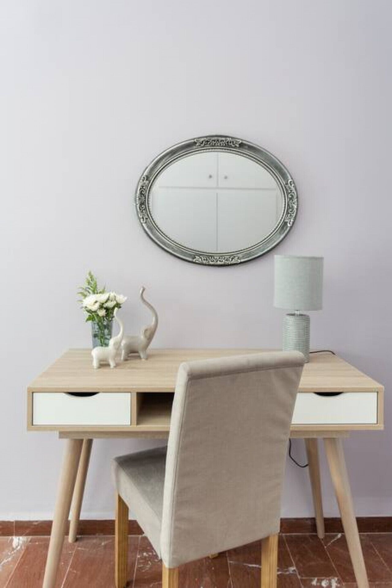 A minimalist desk with a round mirror, a lamp, and decorative items.