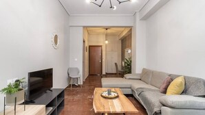 A modern living room with a flat-screen TV, a wooden coffee table, a grey sofa, and a dining area in the background. - Explore History from a Chic Central Apartment (Athina)