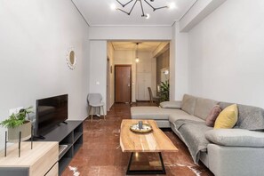A modern living room with a flat-screen TV, a wooden coffee table, a grey sofa, and a dining area in the background. - Explore History from a Chic Central Apartment (Athina)