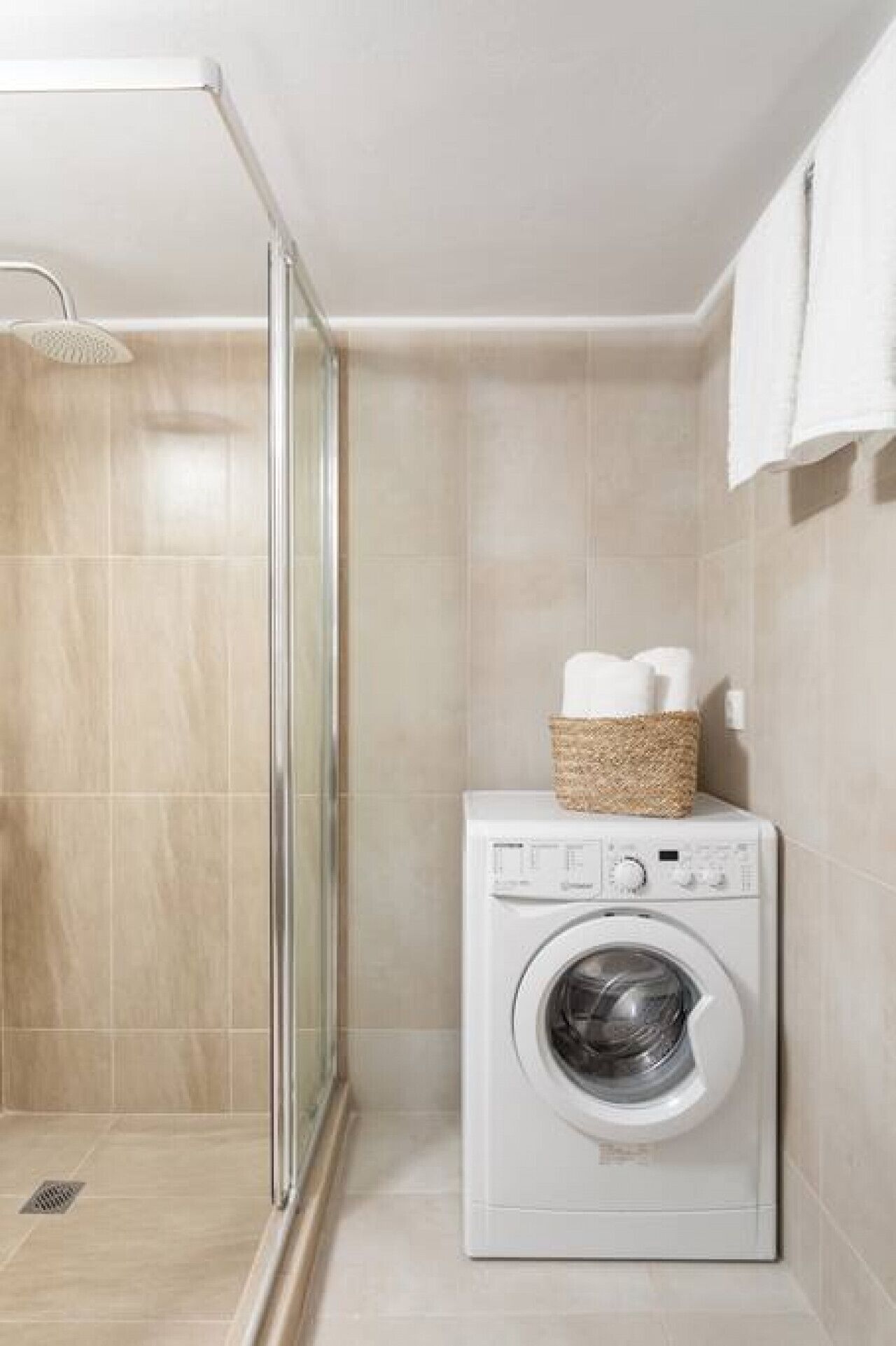 Un espace buanderie compact comprenant un lave-linge et une cabine de douche en verre.