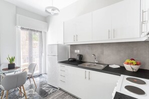 A modern kitchen with white cabinets, a black countertop, a sink, and a stove. There is a potted plant on the left and a bowl of fruit on the right. - Explore History from a Chic Central Apartment (Athina)