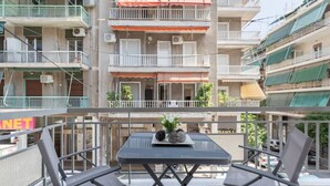 A balcony with two chairs and a table, overlooking a multi-story building with balconies and air conditioning units. - Explore History from a Chic Central Apartment (Athina)