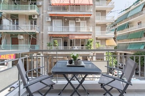 A balcony with two chairs and a table, overlooking a multi-story building with balconies and air conditioning units. - Explore History from a Chic Central Apartment (Athina)