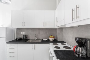 A modern kitchen with white cabinets, a black countertop, a sink, a kettle, a bowl of fruit, and a coffee maker. - Explore History from a Chic Central Apartment (Athina)