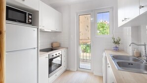 Een compacte keuken met witte keukenkastjes, een inbouwoven, een magnetron en een broodrooster.