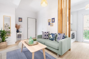 A modern living room with a light green sofa, patterned cushions, a wooden coffee table, and a large window offering a view of greenery. - Modern & Stylish Hideaway Downtown near Acropolis (Athina)