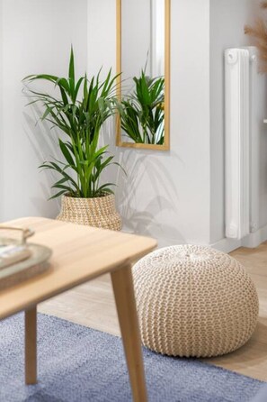 A modern living room with a wooden table, a woven pouf, and two large green plants in woven baskets. - Modern & Stylish Hideaway Downtown near Acropolis (Athina)