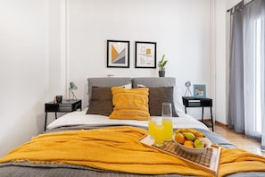 A modern bedroom with a bed, two nightstands, a tray with fruit and juice, and two framed pictures on the wall. - Bright, Modern Retreat Near Acropolis w/ Balcony (Athina)