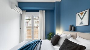 Une chambre d’hôtel avec un lit, une fenêtre avec des rideaux, un climatiseur fixé au mur et un tableau encadré accroché au mur.