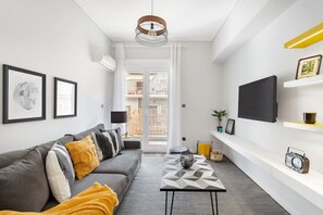 Ett modernt vardagsrum med en grå soffa, ett geometriskt soffbord och en stor TV på väggen.