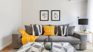 Un salon moderne avec un canapé gris, un plaid jaune et deux œuvres d’art encadrées accrochées au mur.