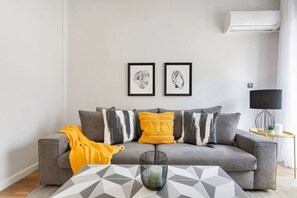 Ett modernt vardagsrum med en grå soffa, en gul pläd och två inramade konstverk på väggen.