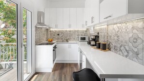 Une cuisine moderne avec des meubles blancs, un four à micro-ondes, une machine à café et une grande fenêtre.