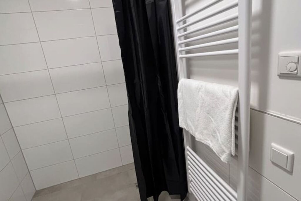 A bathroom with white tiled walls, a black shower curtain, and a towel hanging on a radiator.