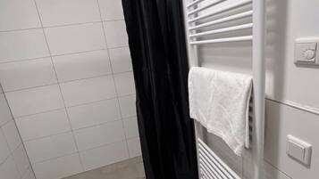 A bathroom with white tiled walls, a black shower curtain, and a towel hanging on a radiator.