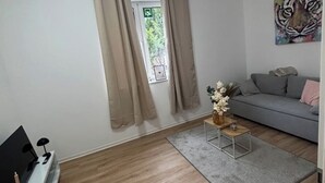 A modern living room with a grey sofa, a small side table with a vase, and a TV on a stand.