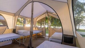 Una tenda con due letti, una panca e vista su palme.