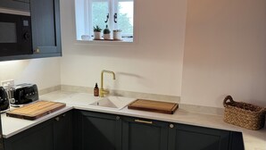 Uma cozinha moderna com armários escuros, bancada branca, piso de madeira em padrão herringbone, luminária pendente e janela com plantas.