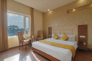 Ein Hotelzimmer mit einem großen Bett, einem hölzernen Kopfteil, einem kleinen Tisch mit Stuhl und Blick auf die Stadt durch das Fenster.