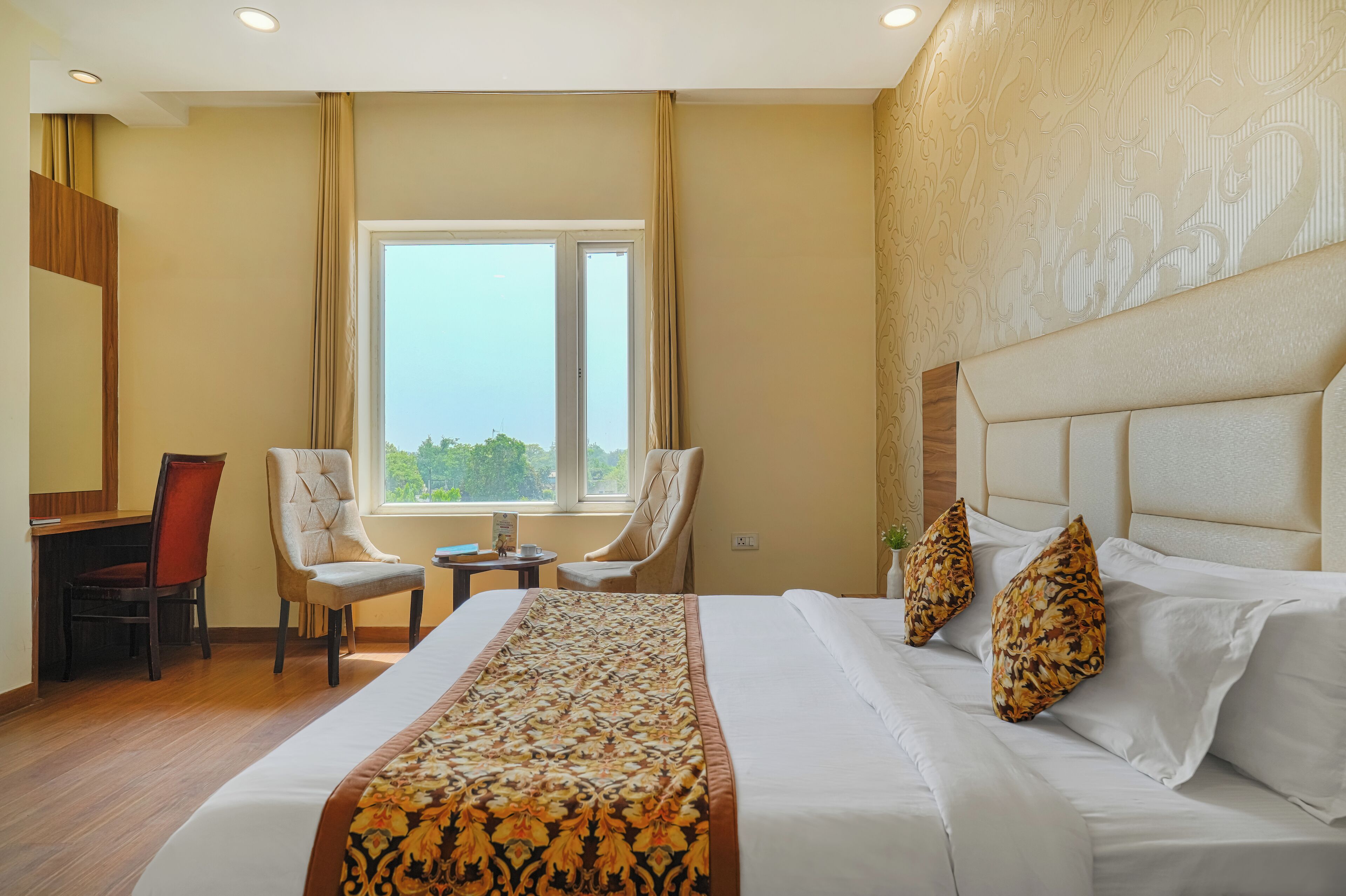 A hotel room with a large bed, two chairs, a desk, and a window with a view.