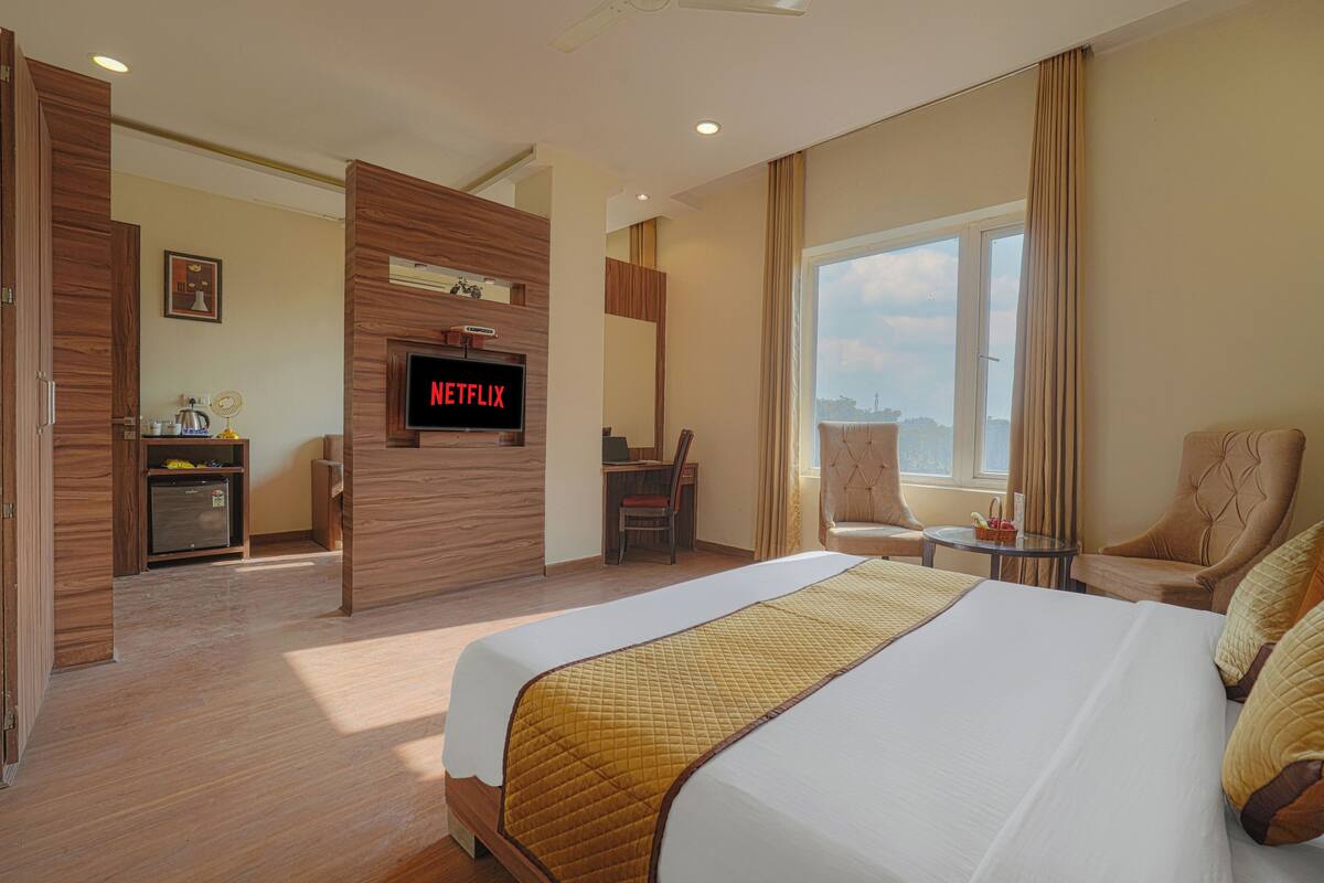 Habitació d'hotel amb un llit, escriptori, cadira, televisió i finestra amb cortines.