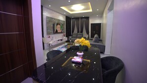 A modern living room with a black marble dining table, a sofa, and a TV mounted on the wall. - Evanluck Luxury Homes (Lagos)