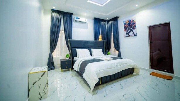 A modern bedroom with a bed, nightstand, and a small table with a plant. - Evanluck Luxury Homes (Lagos)