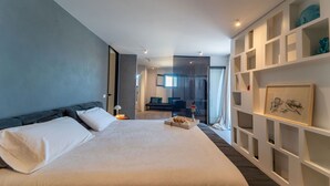 Ein modernes Hotelzimmer mit einem großen Bett, einer integrierten Bücherwand und Blick auf den Flur.