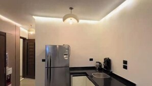 A modern kitchen with a stainless steel refrigerator, a black countertop, and a pendant light. - Modern Deluxe Studio by the Pyramids – Comfort & Style in Giza (Giza Governorate)