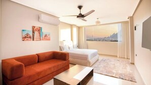 A modern hotel room with a sofa, a bed, a coffee table, and a view of a cityscape. - Modern Deluxe Studio by the Pyramids – Comfort & Style in Giza (Giza Governorate)