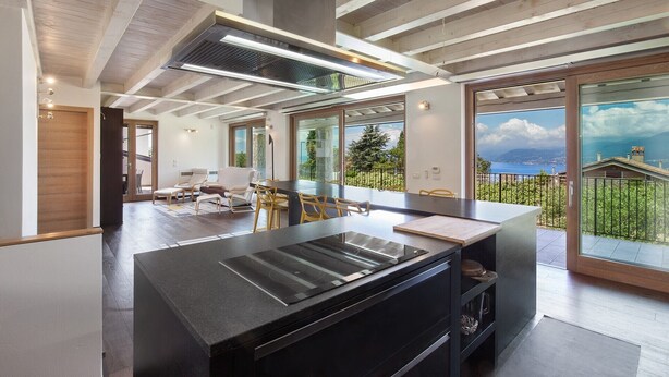 A modern kitchen with a large island, a built-in stove, and a view of the sea through large windows. - Ca' Bosca: Exclusive Lakeview Villa with Private Pool and Rooftop in Albisano (Torri del Benaco)