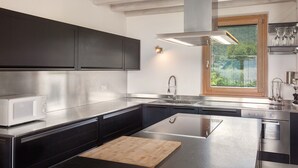A modern kitchen with a central island, stainless steel appliances, and a window with blinds. - Ca' Bosca: Exclusive Lakeview Villa with Private Pool and Rooftop in Albisano (Torri del Benaco)