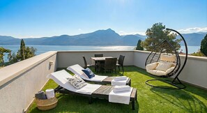 A balcony with two sun loungers, a hanging chair, a table, and chairs. - Ca' Bosca: Exclusive Lakeview Villa with Private Pool and Rooftop in Albisano (Torri del Benaco)