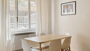 Een kamer met een houten tafel, witte stoelen, een radiator en een raam met gordijnen.
