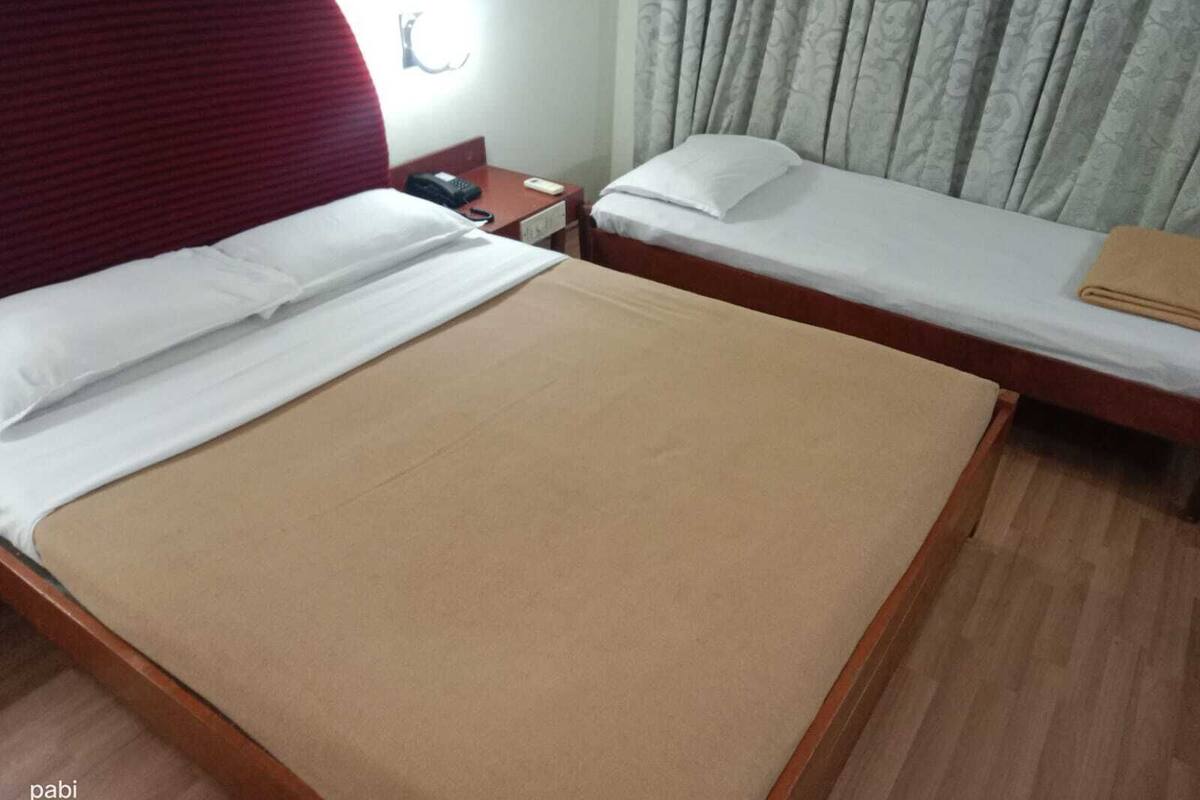 A hotel room with two single beds, a wooden floor, a red headboard, a nightstand with a phone, and a curtain.