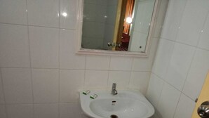 A small bathroom with a white sink, a mirror above it, and a door to the right. - Hotel Goutham Manor (Chennai)