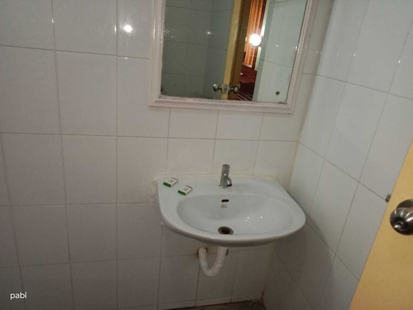 Une petite salle de bain avec un lavabo blanc, un miroir au-dessus et une porte sur la droite.