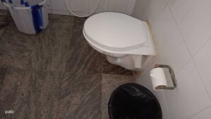 A bathroom with a toilet, a bidet, a trash bin, and a toilet paper holder. - Hotel Goutham Manor (Chennai)