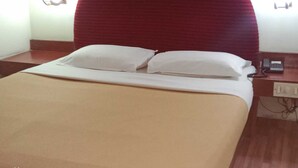 A hotel room with a large bed, two pillows, a bedside table with a phone, and a wall-mounted light fixture. - Hotel Goutham Manor (Chennai)