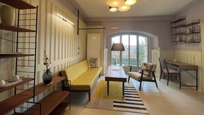 Uma sala de estar moderna com sofá, mesa de jantar e mesa de centro. Há prateleiras com objetos decorativos e uma janela com vista.