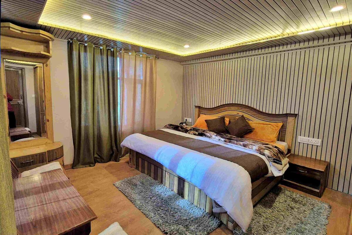 A bedroom with a wooden bed, a bedside table, a mirror, and a window with curtains.