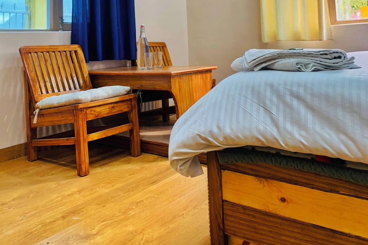 A bedroom with a bed, wooden chairs, a small table, and a window with curtains.