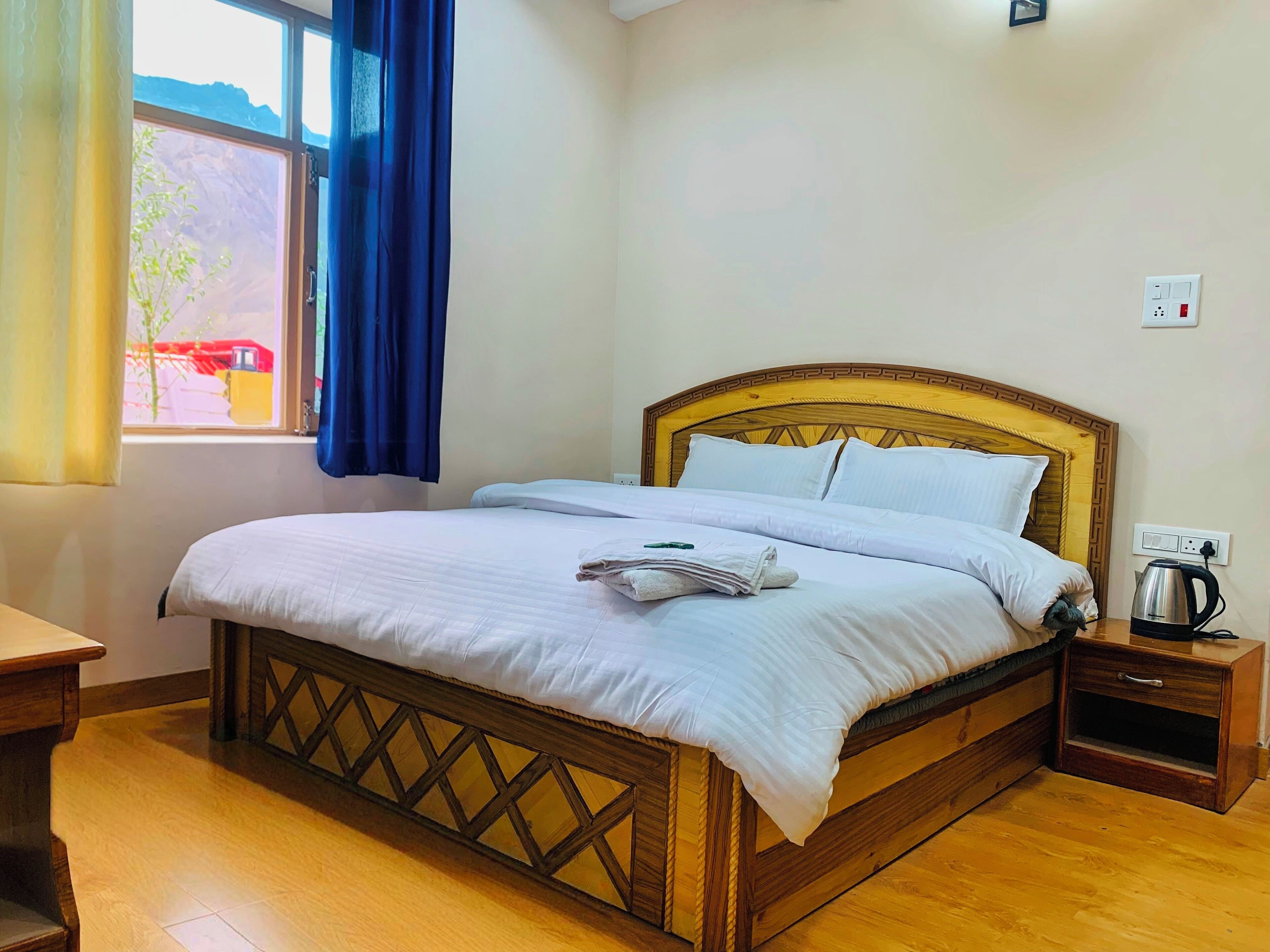 Una cama bien hecha con sábanas blancas, cabecera de madera y mesita de noche con tetera.